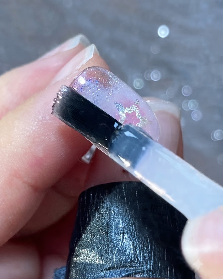 A nail brush applying a smooth layer of clear top coat over decorated nails.