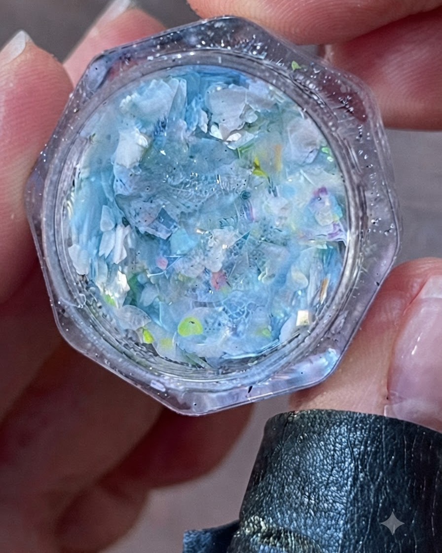 A close-up view of an open jar filled with iridescent blue and white flakes and glitter.