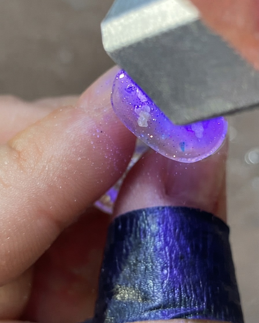 A hand under a purple UV/LED nail lamp curing a decorated nail design.