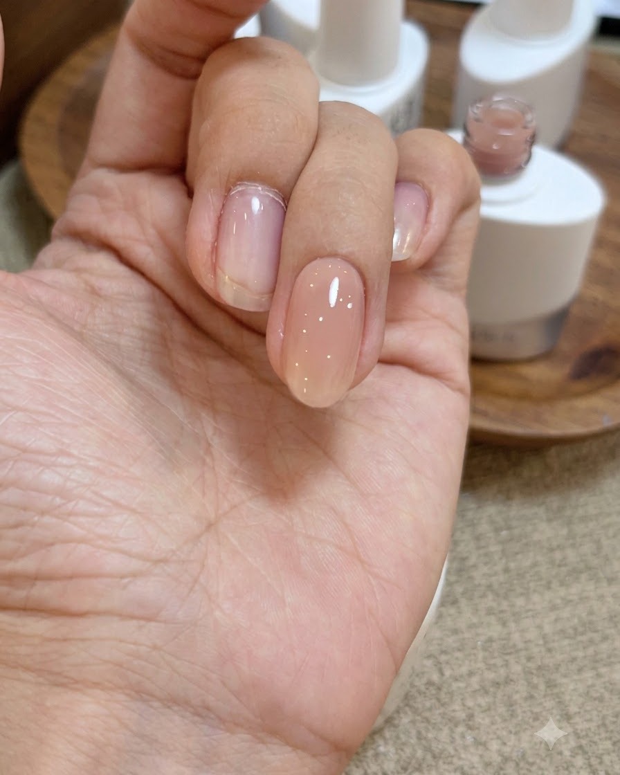 A close-up view of a hand with a wet, glossy layer of clear base gel applied over the nude pink nail.