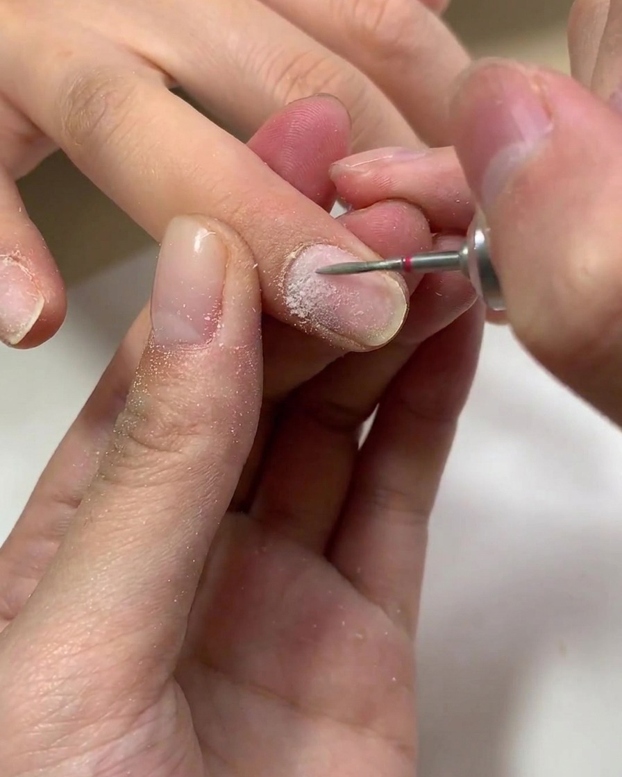 A brush applying a clear layer of gel base coat onto a natural fingernail.