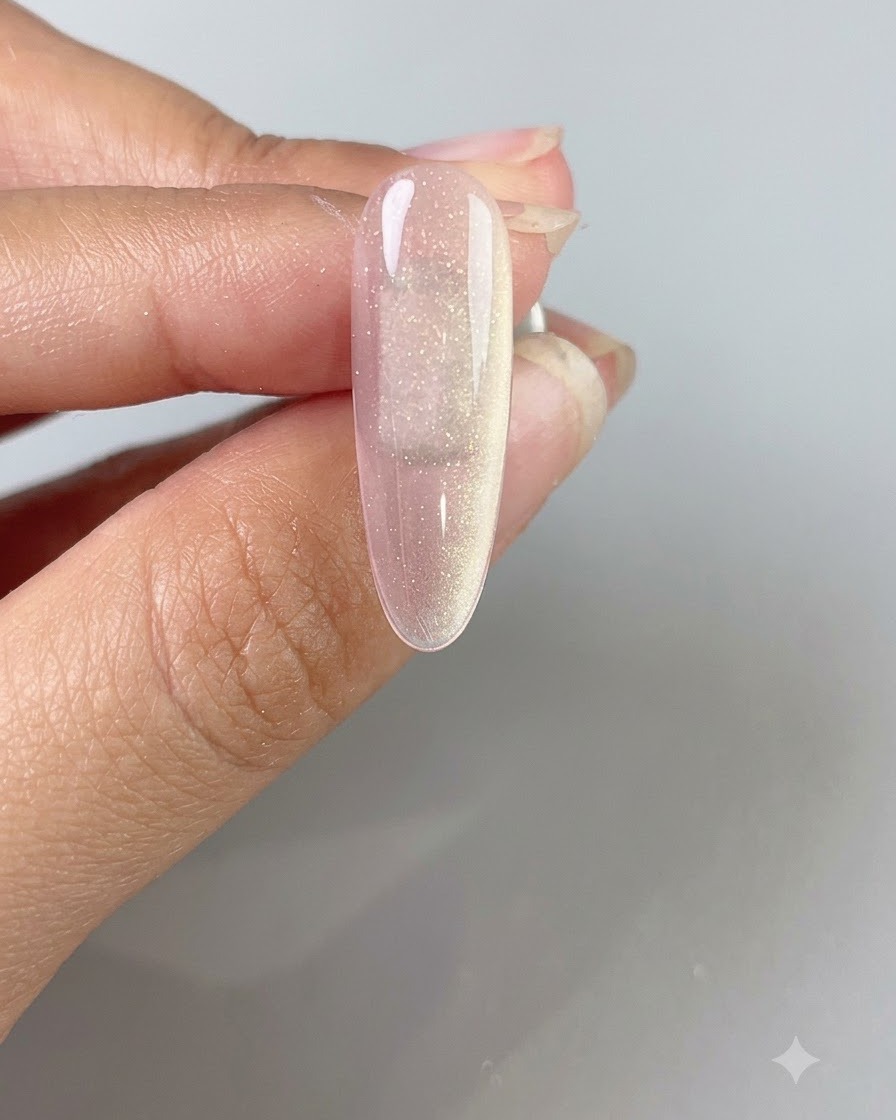 A hand holding a magnetic wand over a pink translucent cat-eye gel nail to create a wide glowing light beam.