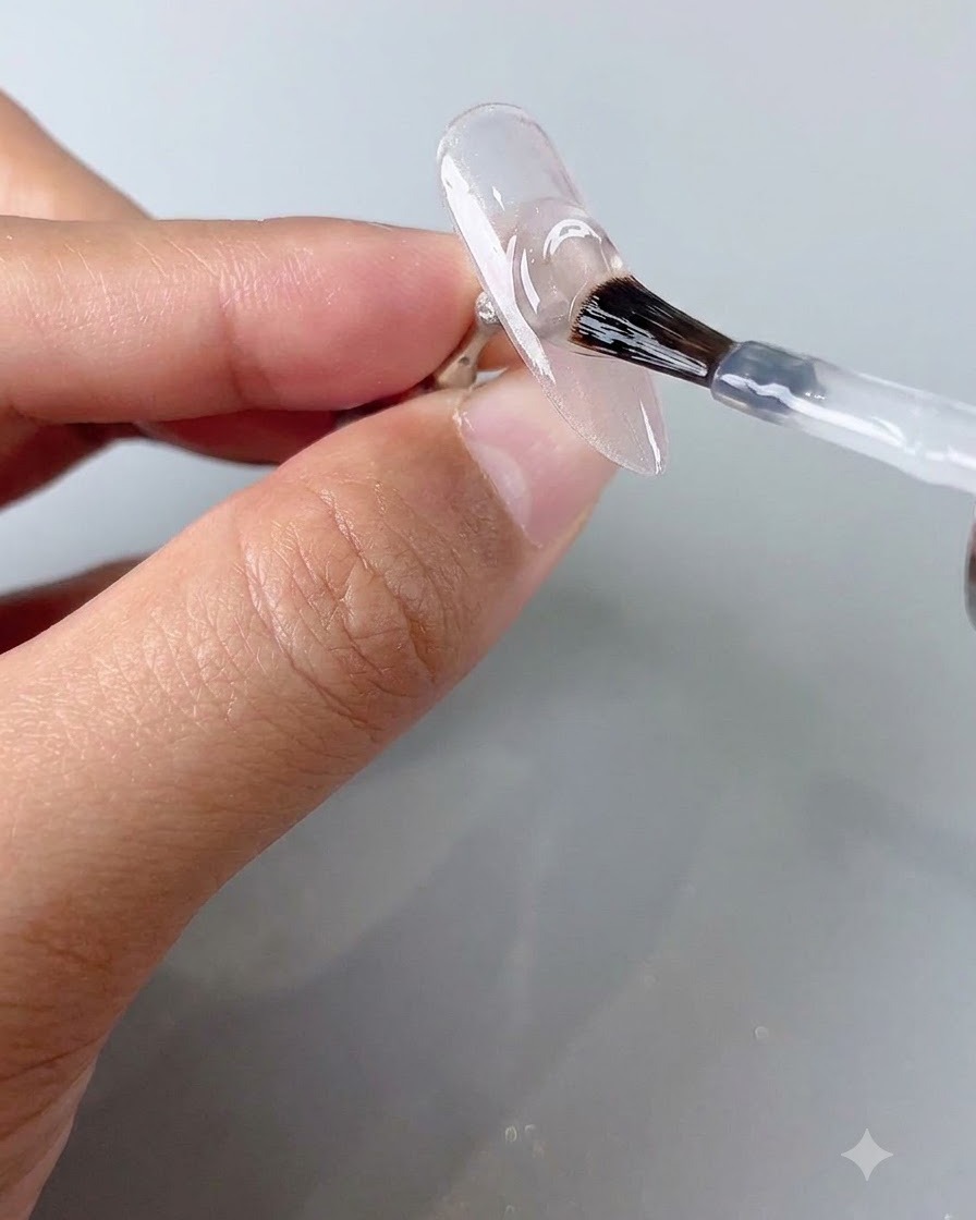 A nail brush applying a clear top coat layer onto a cured cat-eye nail.