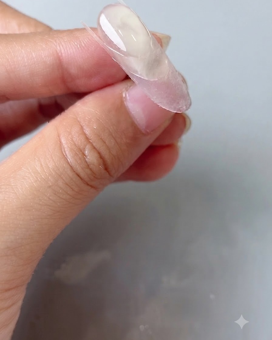 A silicone nail tool pressing down a clear guide sticker on an oval nail.