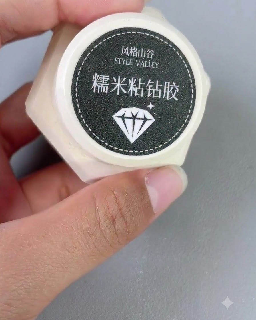 A small container of Style Valley sticky diamond gel held in a hand next to a nail brush.