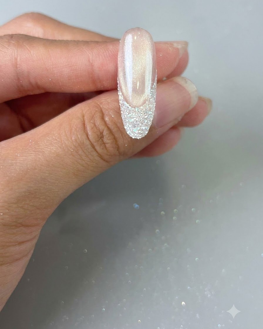 A hand holding a finished nail with a glitter French tip, ready for final curing.