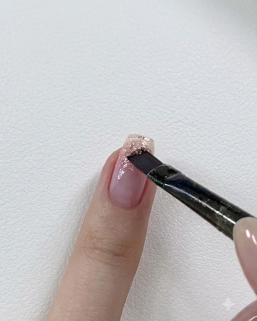 A nail brush layering a darker pink glitter gel over the tip of a partially glittered nail.