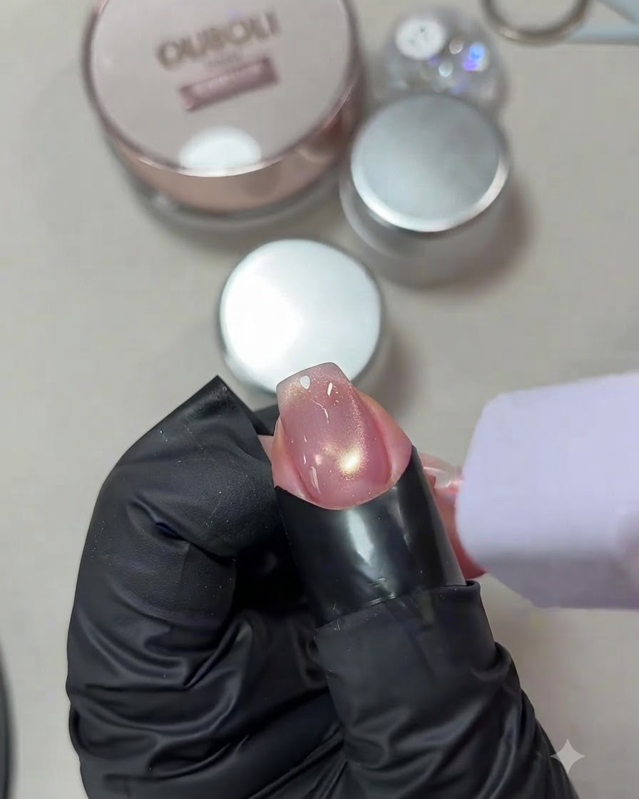 A fingernail with a glowing cat-eye gel design being cured under a small, handheld purple UV/LED lamp.