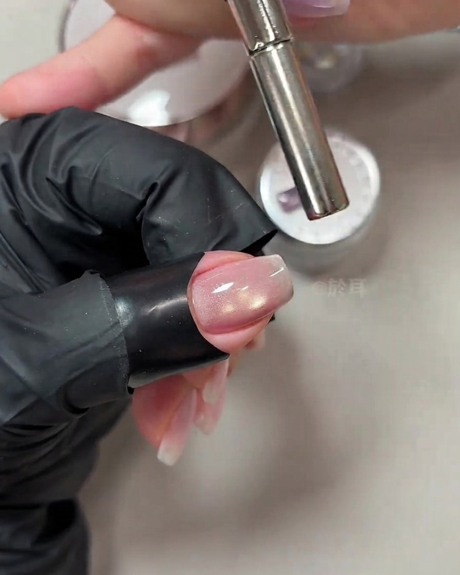 A cylindrical magnetic wand held close to the tip of a manicured nail to manipulate cat-eye shimmer.