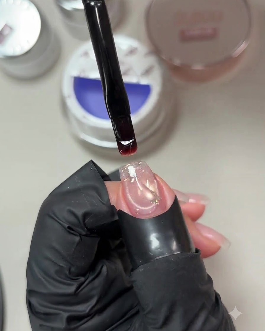 A brush holding a drop of pale purple-blue builder gel above a prepped nail with an embedded sequin.