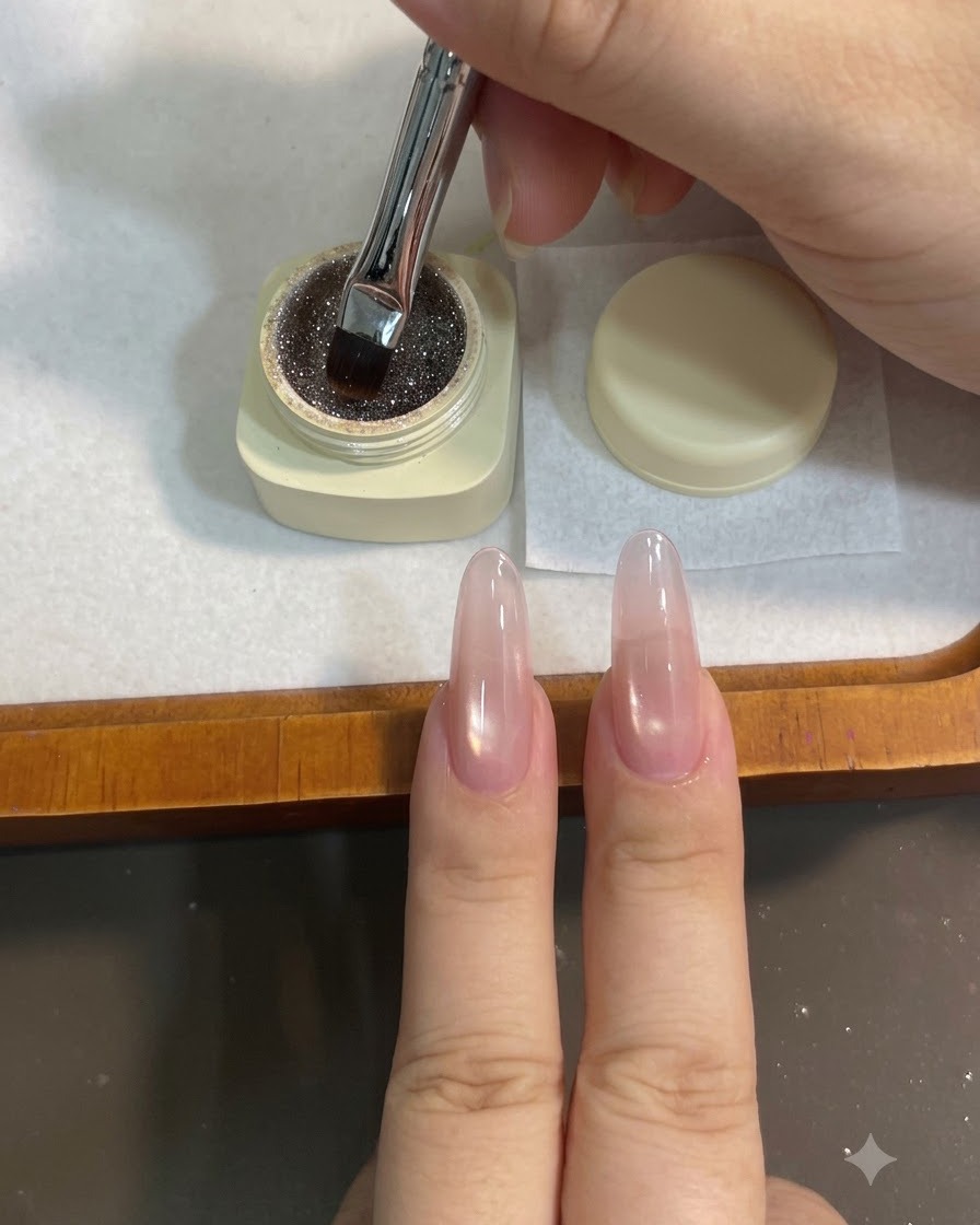 A flat gel brush dipping into a small pot of sparkly brown coffee-toned glitter gel.