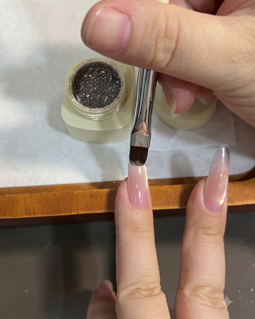A flat brush applying sparkly brown glitter gel to the tip of an almond nail, sweeping it down to create an ombre effect.