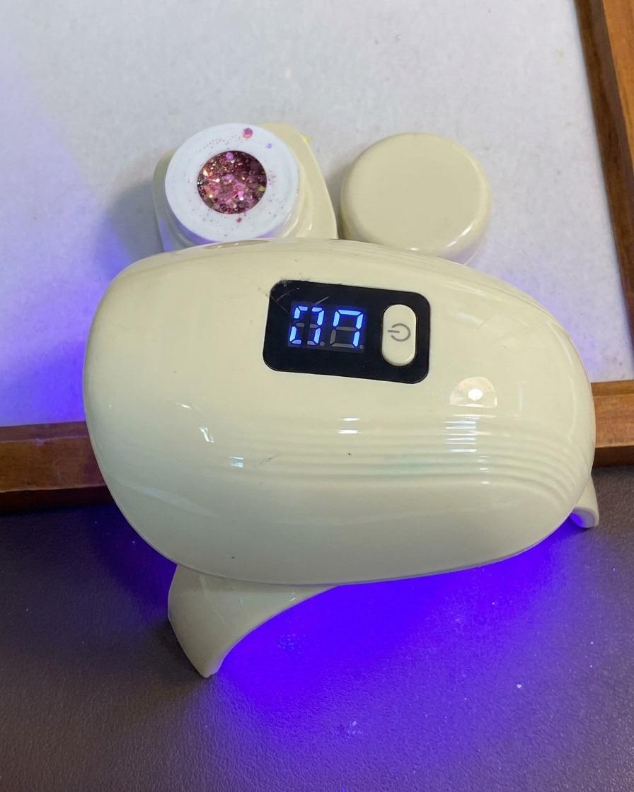 A hand placing fingers under a compact blue and white LED nail curing lamp.