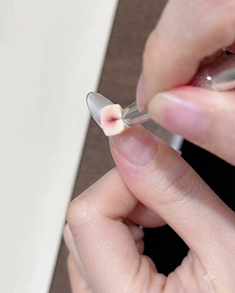 A close-up of a small wedge sponge dabbing nude concealer gel onto the natural nail near the smile line.