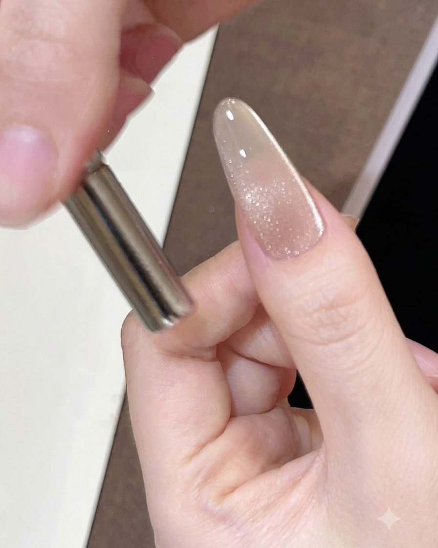 A cylindrical magnet held close to the side of a painted nail to move the magnetic shimmer.