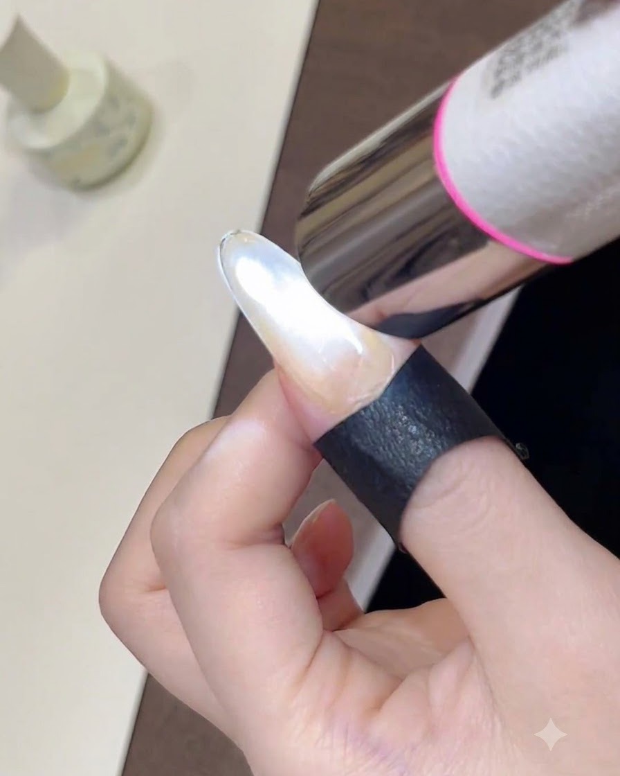 A close-up of a handheld mini UV lamp curing a freshly styled, shimmering cat-eye gel polish on a fingernail.