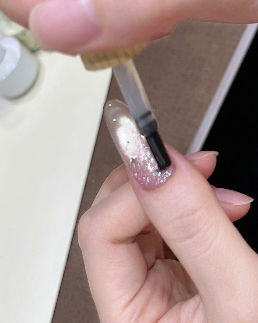 A brush applying a glossy clear top coat over the decorated gradient nail.