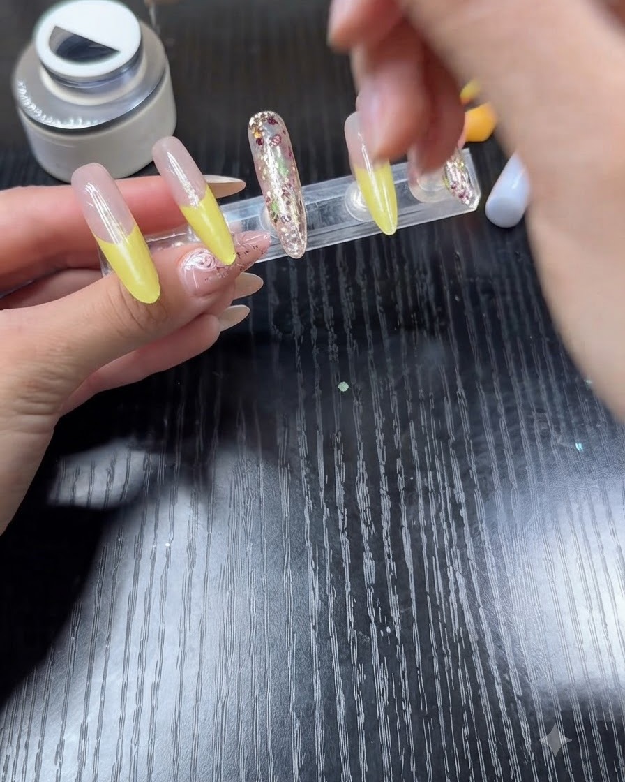 A nail polish brush applying clear top coat over a nail featuring a bright yellow French tip.