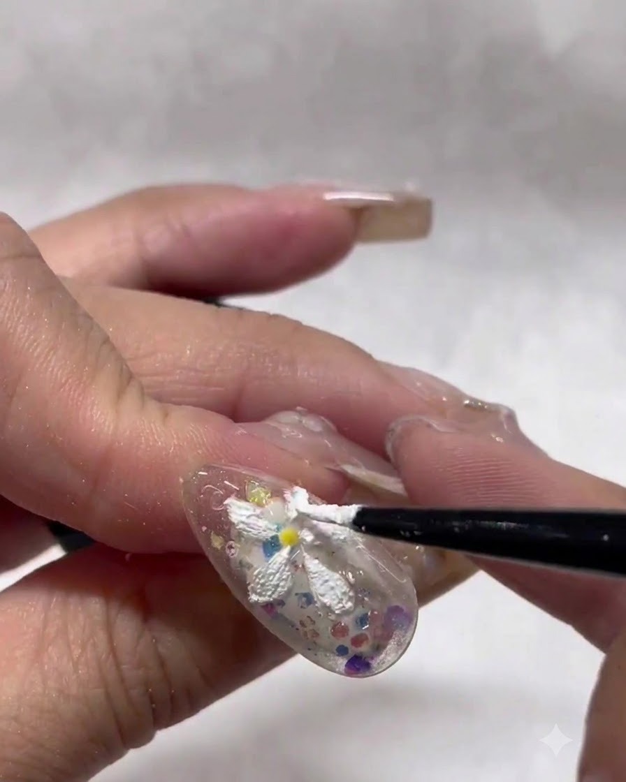 A fine liner brush carefully shaping and tidying the edges of white textured daisy petals on a nail.
