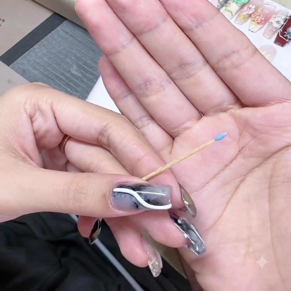 A toothpick held in a hand with a tiny blue gel bead on its pointed tip.