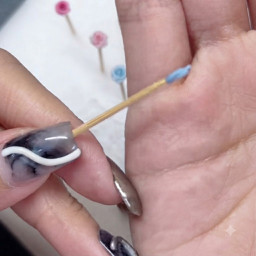 A close-up of a tiny blue sculpted petal wrapped around the tip of a wooden toothpick.