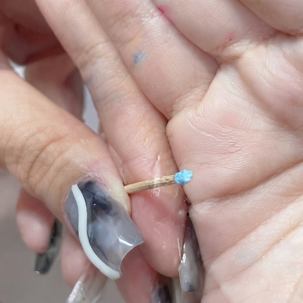 A tiny closed blue rosebud sculpted on the end of a toothpick.