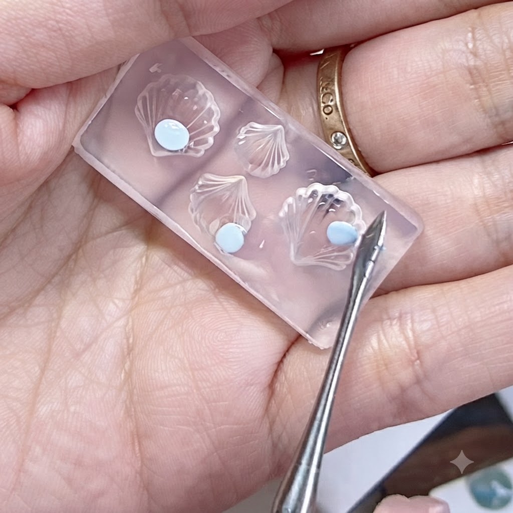 A silicone mold held in a hand with flattened blue gel beads and a sculpting tool nearby.