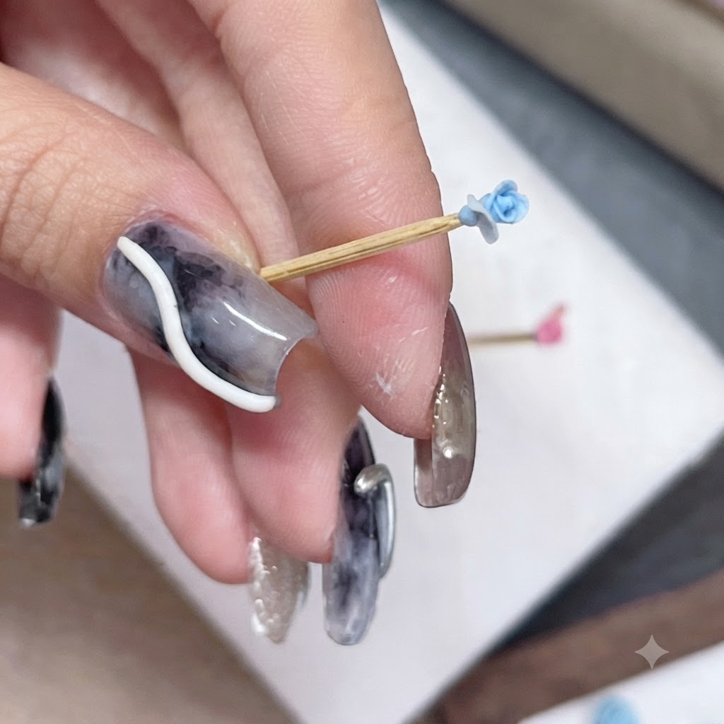 A small blue rose bud on a toothpick held between fingers, showing new petal placement.