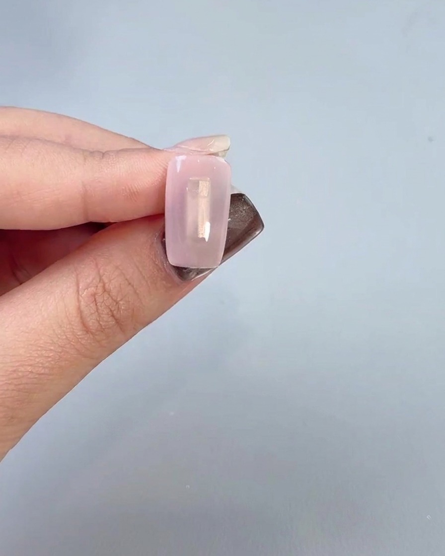 A close-up of a hand applying a clear base coat gel onto a nail surface with a brush.