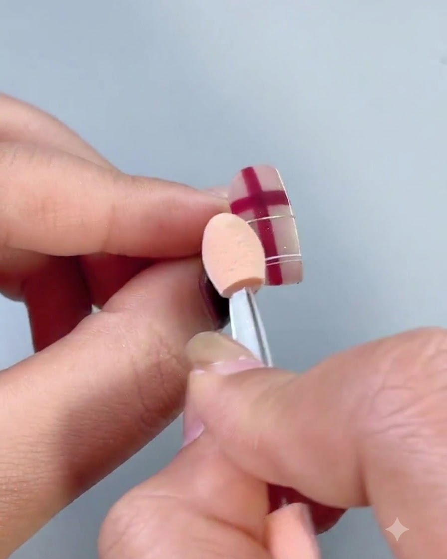 A fluffy white dusting brush sweeping loose metallic powder particles off a decorated nail.