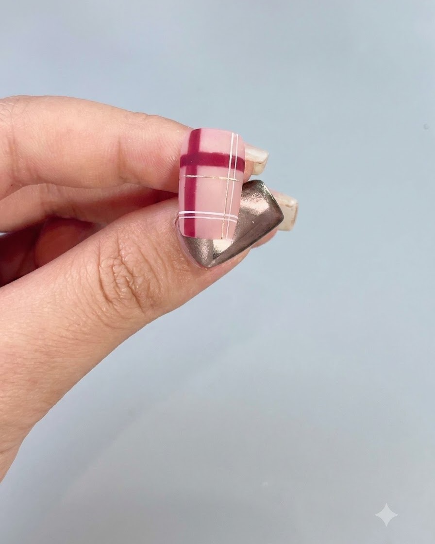 A close-up of a decorated nail featuring a red and white plaid pattern with gold accents.