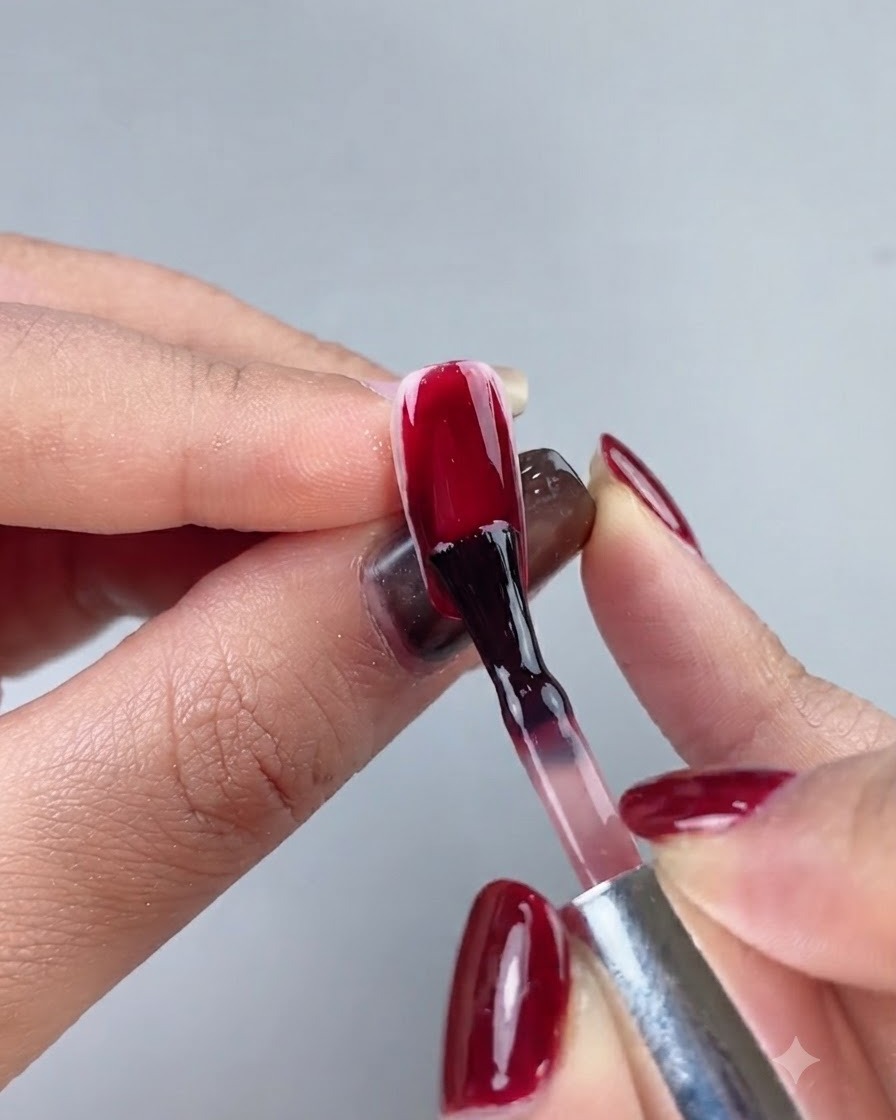 A nail brush applying a deep ox blood red gel polish onto a full nail extension.