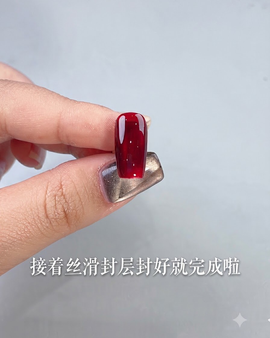 A single nail finished with glossy ox blood red gel polish held by a finger against a light background.