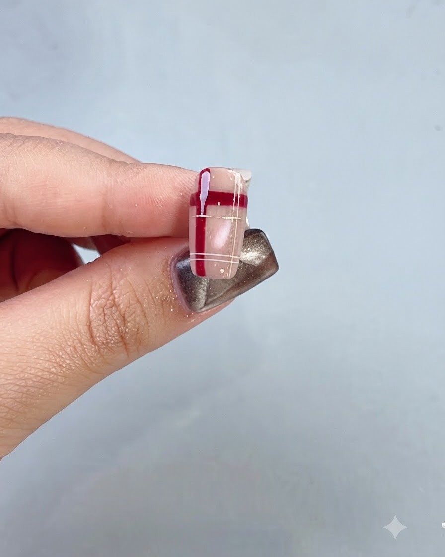 A close-up of a completed nail featuring a red crystal lattice and plaid design.