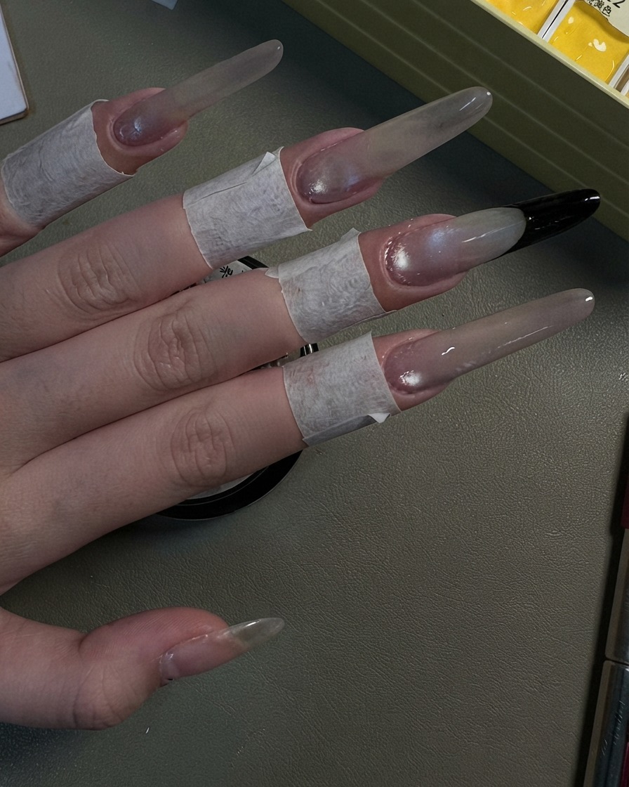 A hand showing four long stiletto nails finished with a pearlescent grey cat-eye shimmer look.