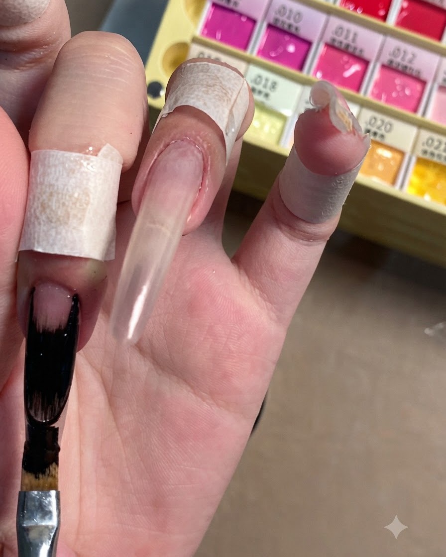 A flat nail art brush applying opaque black gel polish to the elongated tip of a clear stiletto nail.