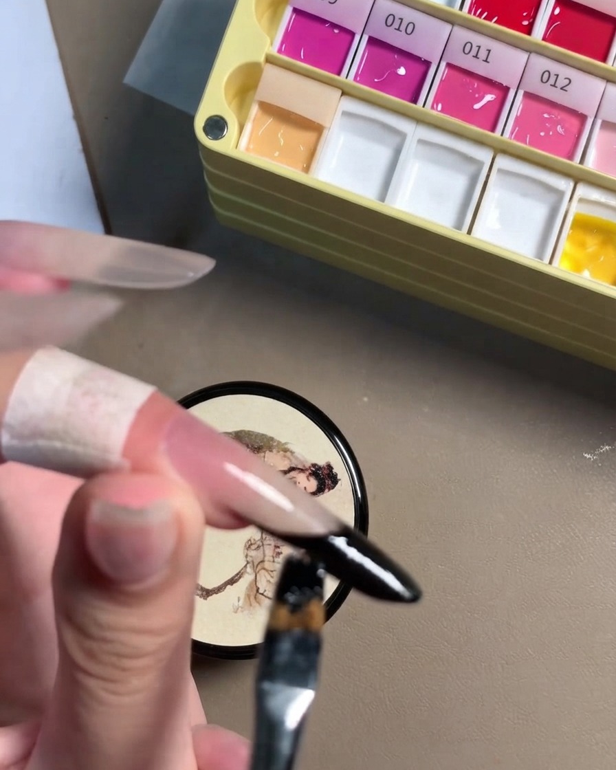 A close-up view of a detail brush perfecting the black gel line on a stiletto nail edge.