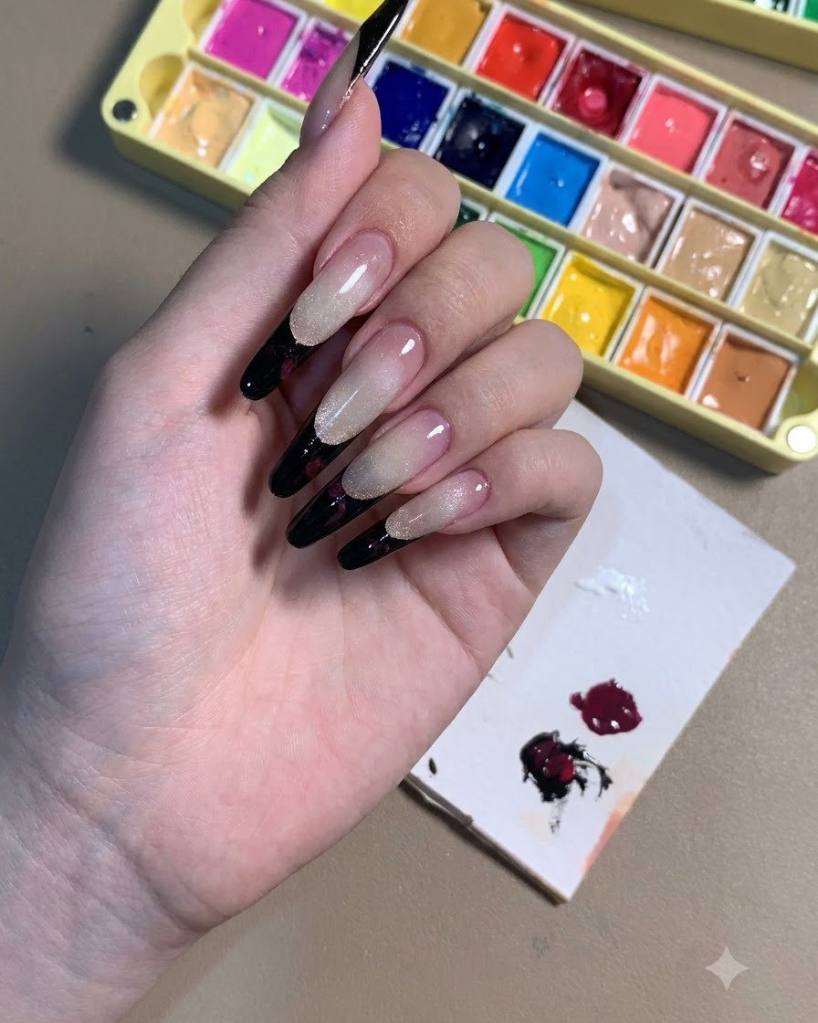 A hand displaying stiletto nails with black French tips and dark plum rose outlines.