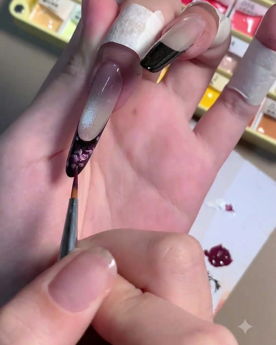 A fine liner brush applying light pink gel strokes over a dark plum rose base on a fingernail.