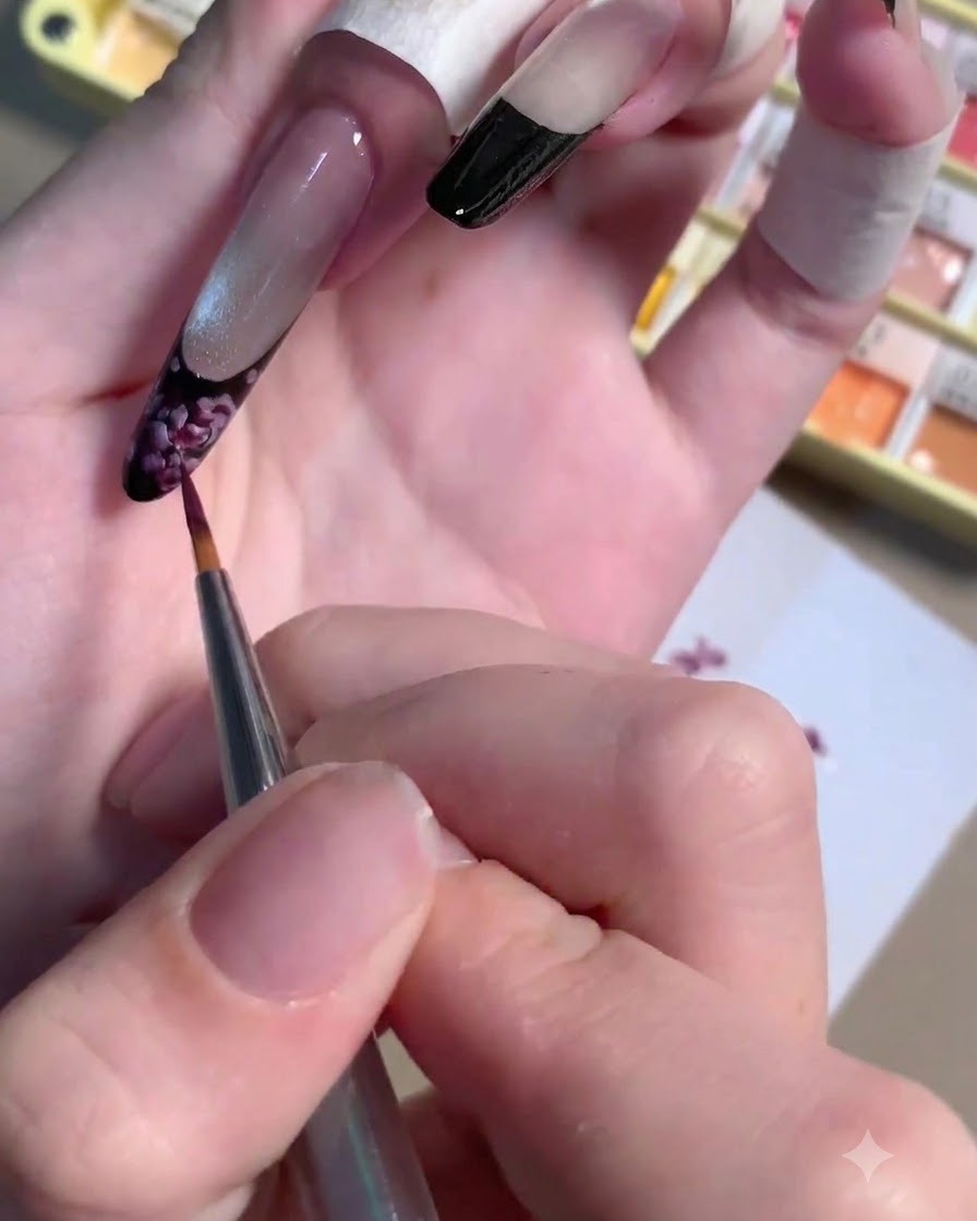 A thin liner brush applying a small dot of dark plum gel to the center of a painted rose.