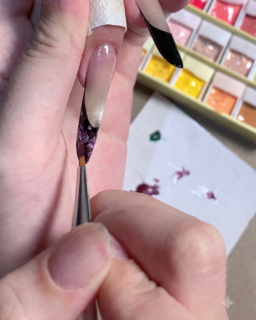 A close-up of a detailing brush refining the dark center of a floral nail design.