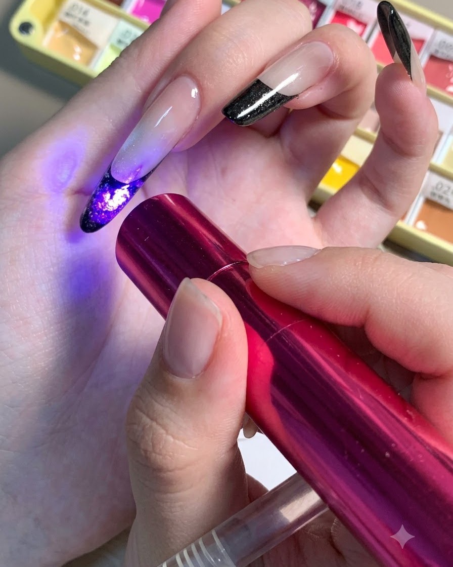 A mini red UV/LED lamp being held over a nail to cure the dark center details of a floral design.