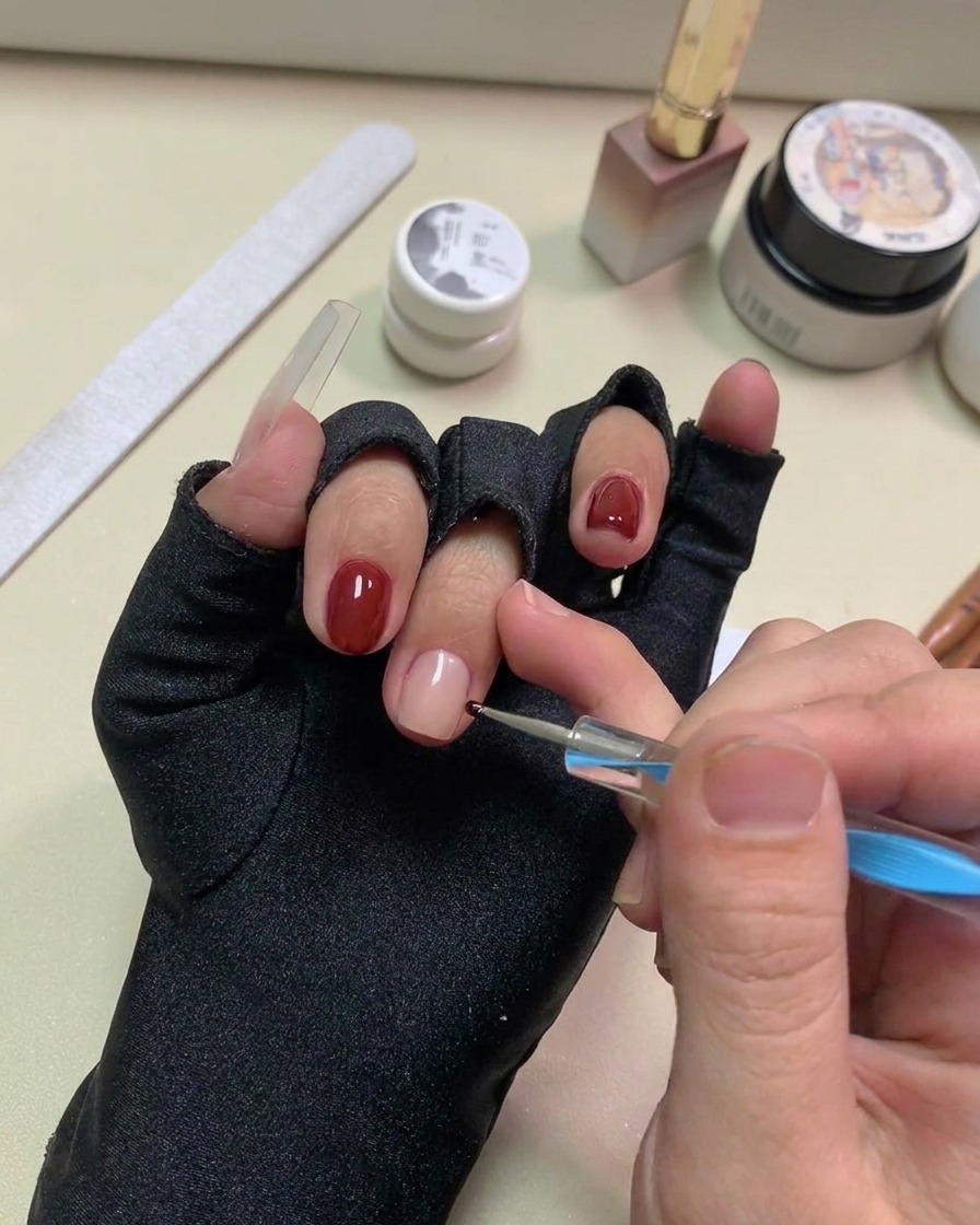 A dotting pen placing small black gel dots onto the nude nail surface.
