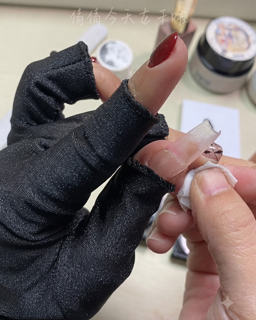A close-up of a hand wiping a finger with a cleansing pad near prepped nail art.