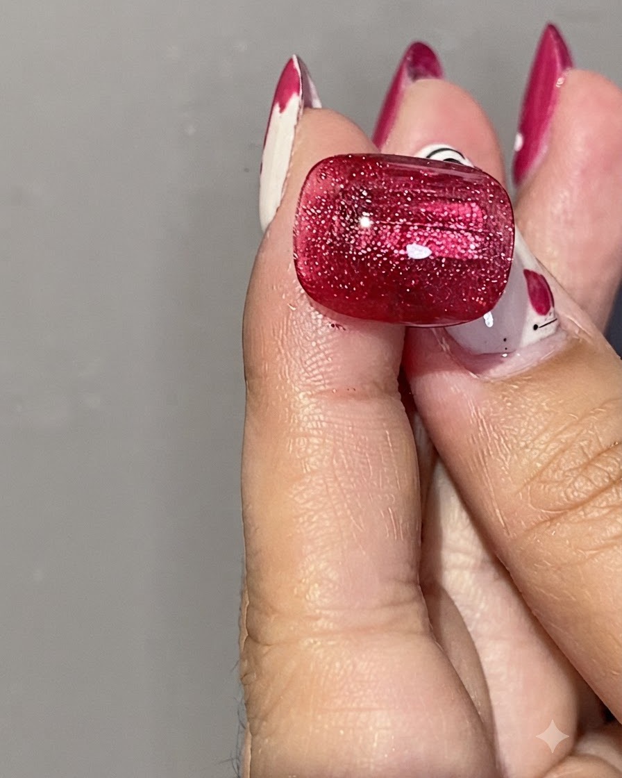 A close-up of a hand holding a silver cylindrical magnet near a glossy red cat eye gel nail to shape the magnetic shimmer.
