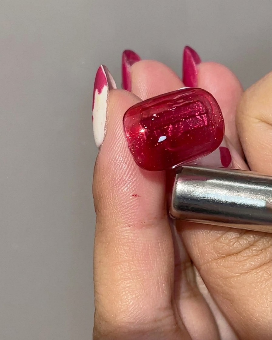 A close-up view of a cured red cat eye gel nail showing a deep crimson base color with a concentrated magnetic light stripe.