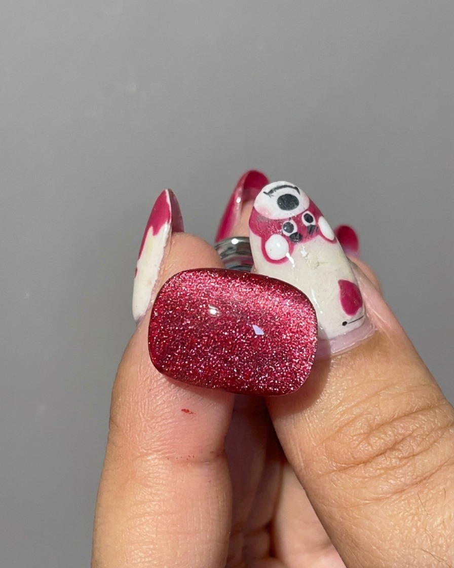 A close-up of a silver cylindrical magnet being held near the edges of a wet red cat eye gel nail to shift the glitter particles.