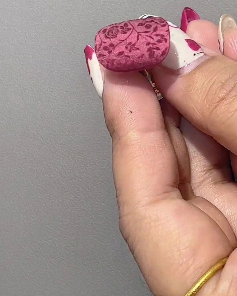 Close-up of a manicured nail displaying a transferred red floral pattern on an uncured glossy base.