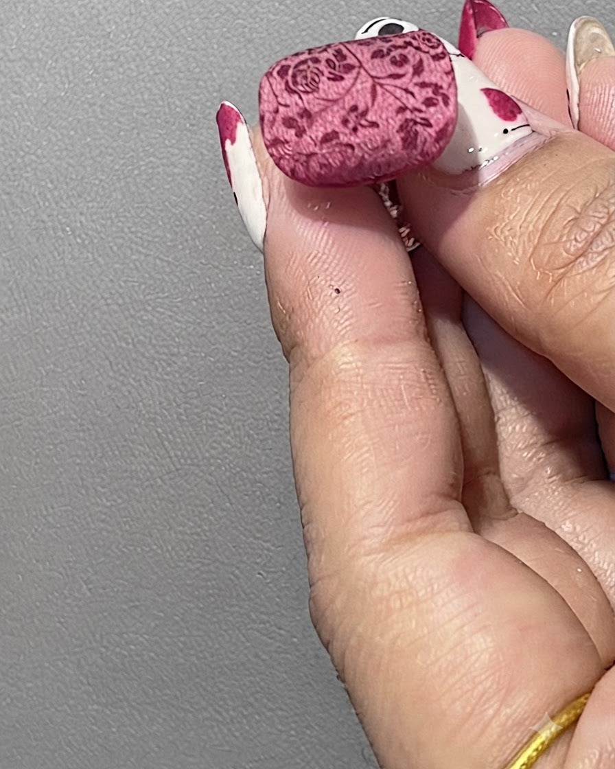 A manicured nail positioned under a curing light to set the powder-coated floral design.