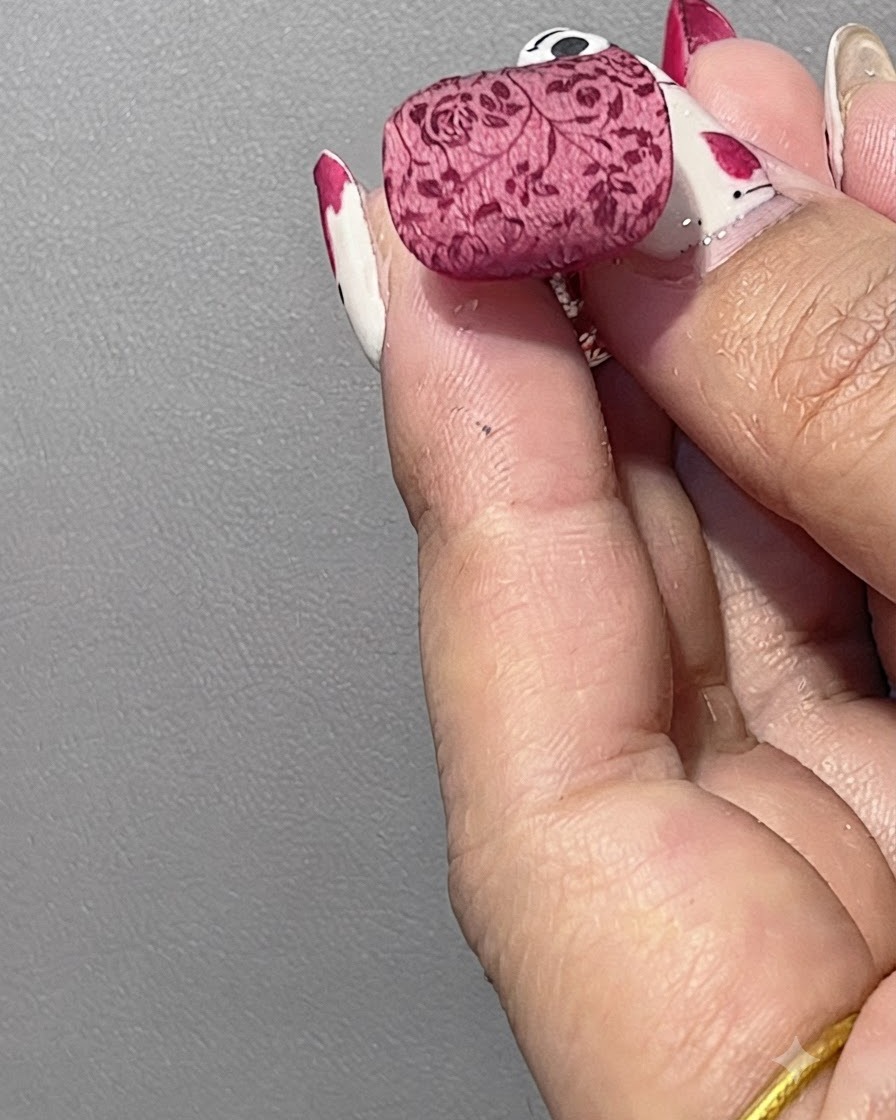 A fluffy brush sweeping away loose white powder from a finished nail showing a soft misty floral pattern.